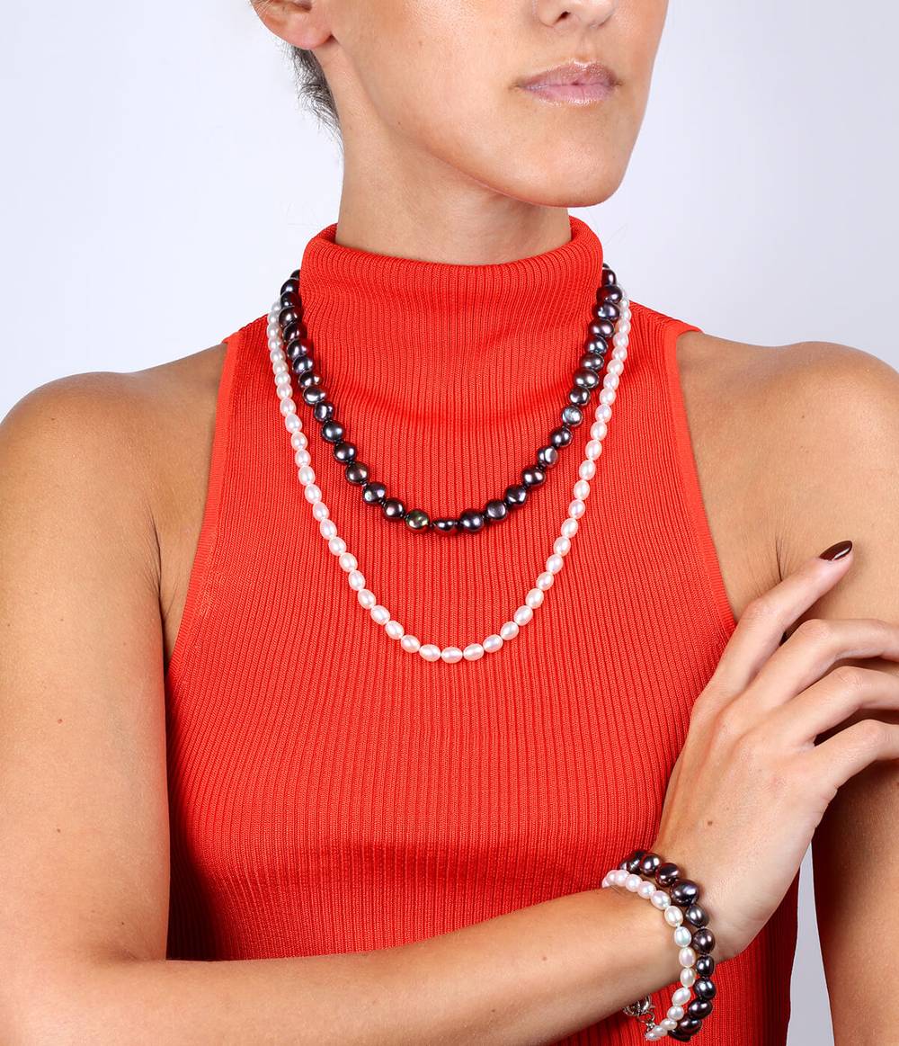 A woman with a red top is wearing a double strand white and peacock pearl necklace and bracelet.