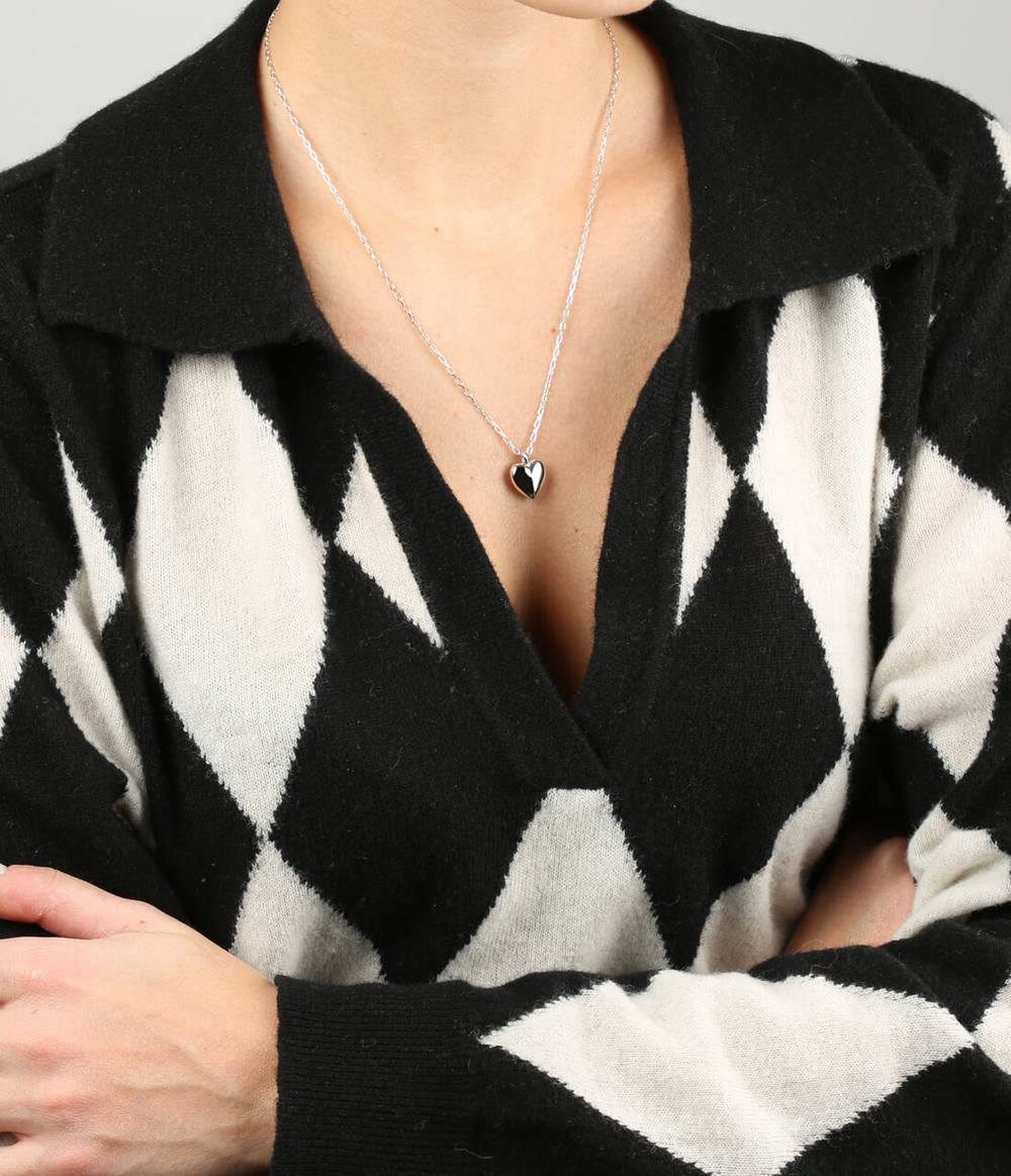 A woman with a black and white jumper is wearing a Heart silver pendant on a silver chain