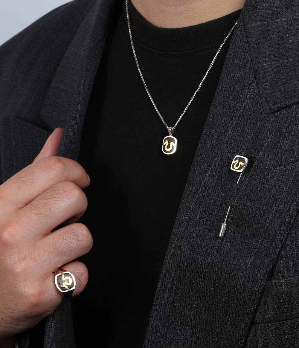 A man wearing a blazer is also wearing an inlaid London Oak silver with a diamond signet ring, necklace and lapel pin. They all have a gold river shaped line in the centre.