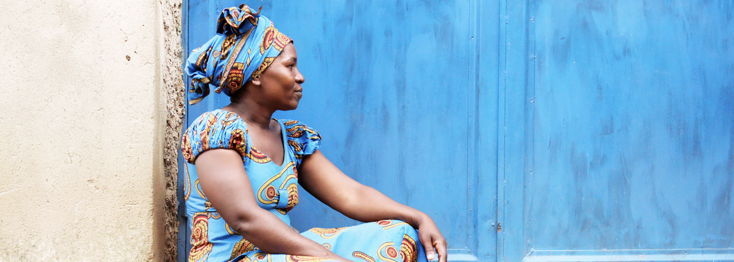 Sitting woman in Rwanda in front of a bright blue wall. 