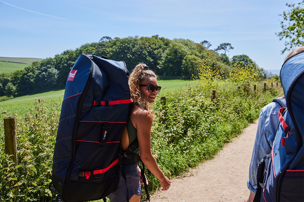 woman carrying paddle board bag whilst walking through a rural path