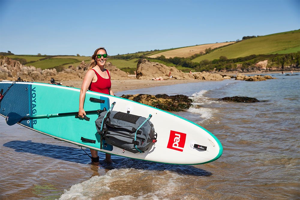 Woman holding A Red Paddle Co Voyager Paddle Board While standing in the sea