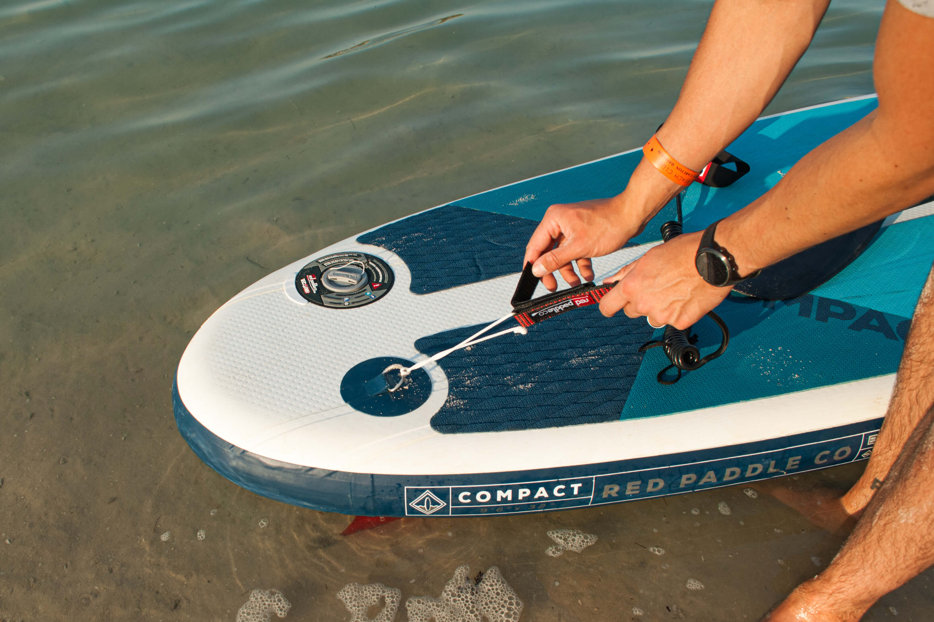Man Attaching A SUP Leash To A Red Compact Paddle Board