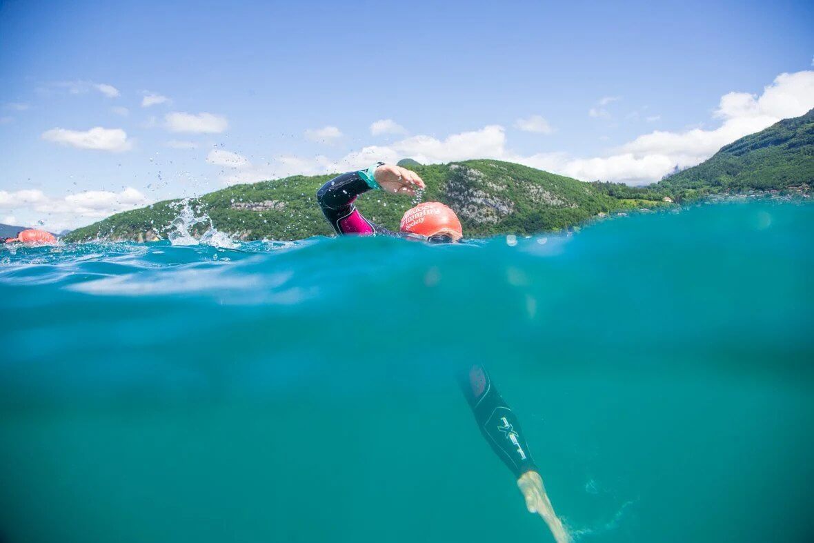 person open water swimming wearing a wetsuit and a pink swim cap 