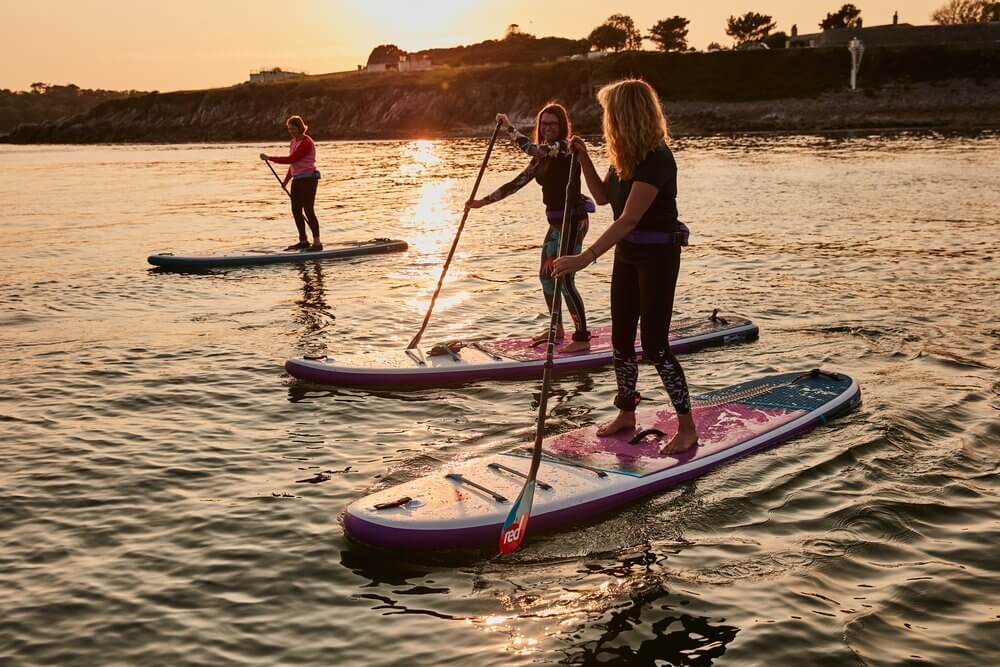 3 women paddling on Red inflatable paddle boards off the Dorset coast at Dusk