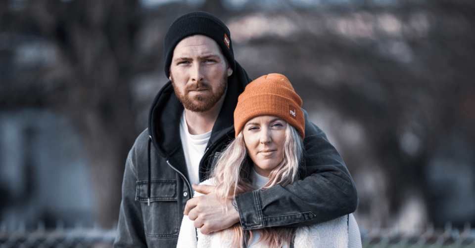couple wearing cuffed knitted beanies in charcoal and orange