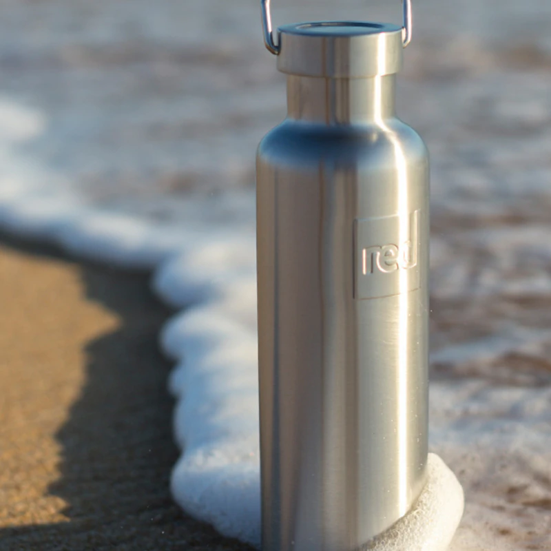 Insulated stainless steel water bottle on the beach near the sea