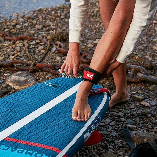 Person attaching Red Original coiled SUP leash to ankle