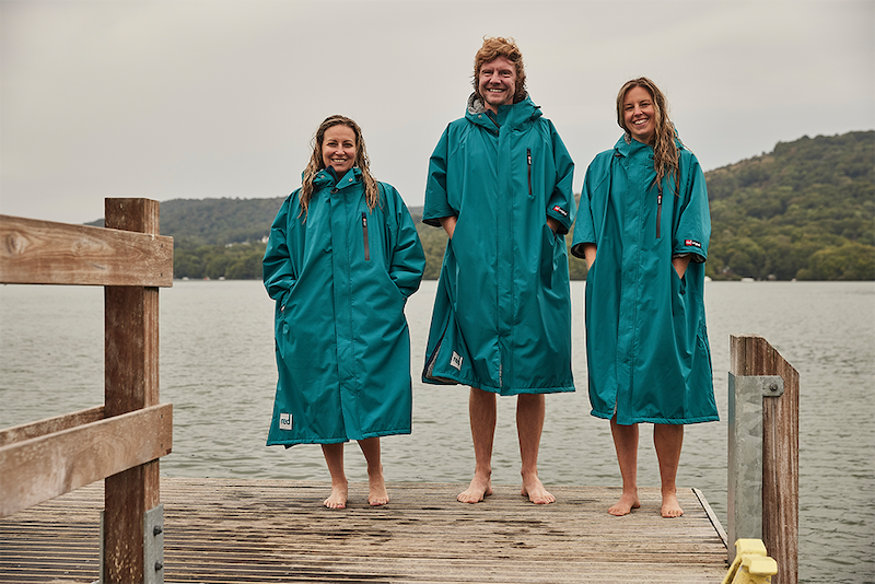Three people standing on platform near lake wearing Red Original waterproof changing robe