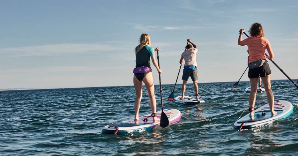 Three people paddle boarding in the sea wearing Red Original personal floatation devices 