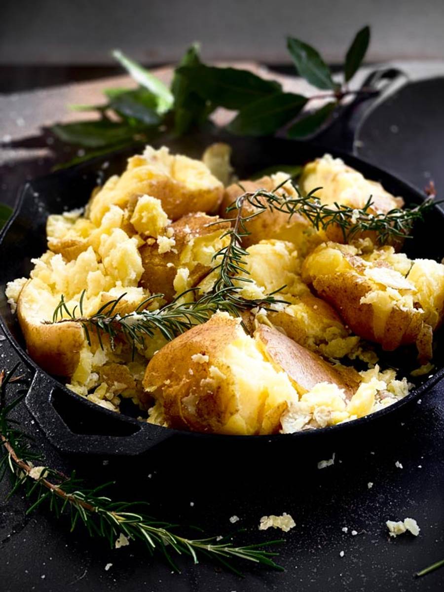 Smashed boiled potatoes in a pan with herbs