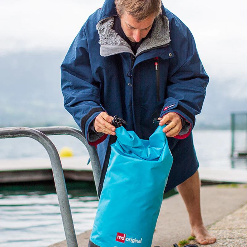 Man holding Red Original waterproof roll top dry bag in aqua blue