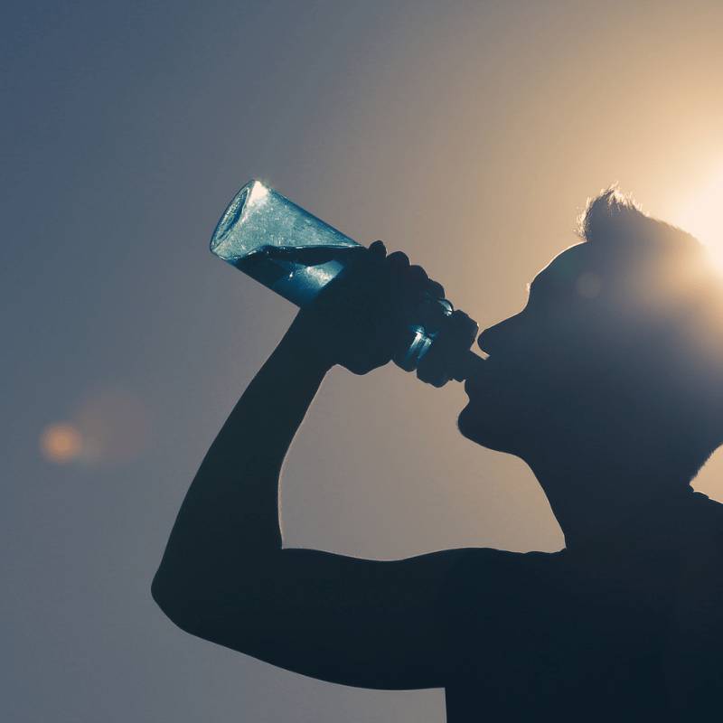 man standing outside in a silouette shadow from the sun whilst drinking from a bottle of water