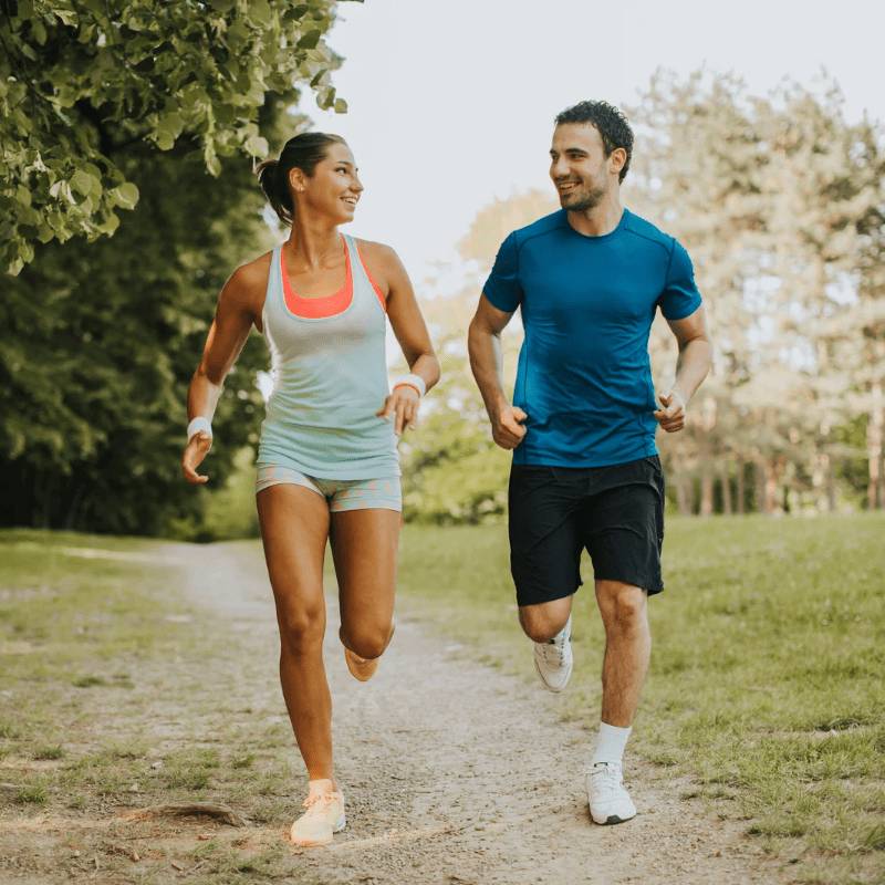 man and woman wearing sports clothing running together outside in a park on a gravel trail