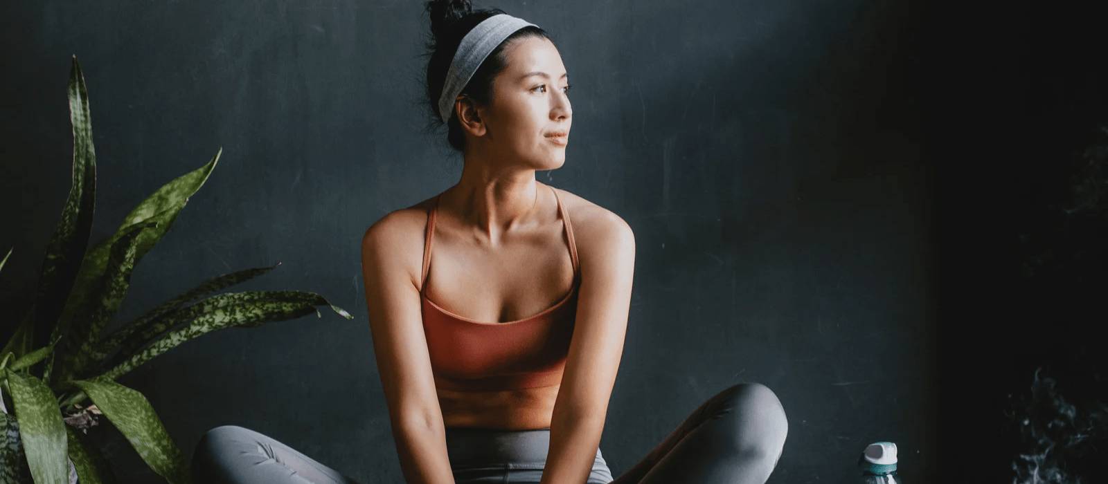 women performing a seated yoga post whilst sitting on a yoga mat and looking into the distance as if contemplating and relaxing in that moment at the same time