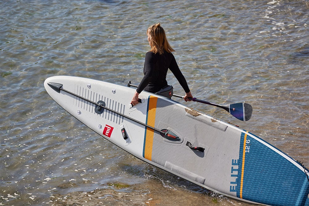 Woman carrying Red 12’6” Elite MSL inflatable paddle board into the sea