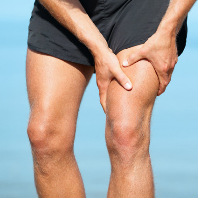 the image shows a runner wearing grey running shorts crouched over and holding the muscles above the knee as if in pain as a result of a sporting injury
