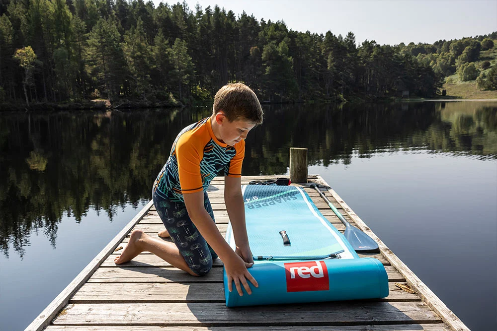 Young boy rolling out paddle board by a lake
