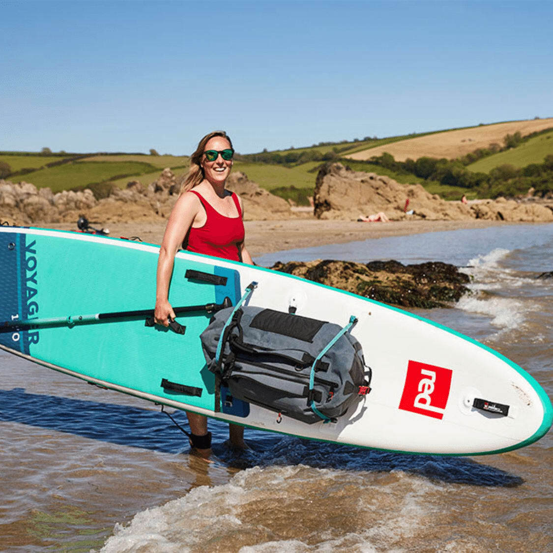 Woman on a beach holding a Red Paddle Co Paddle Board with a deck bag strapped to it