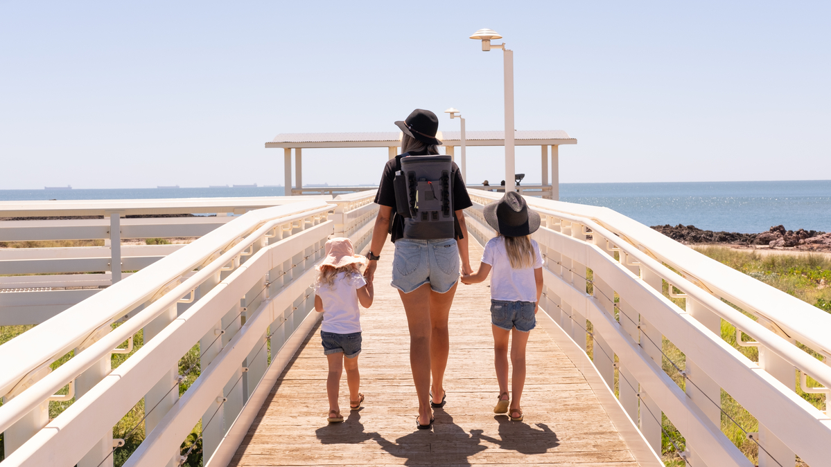 Mother with cool bag and Daughter walking down boardwalk holding hands. 