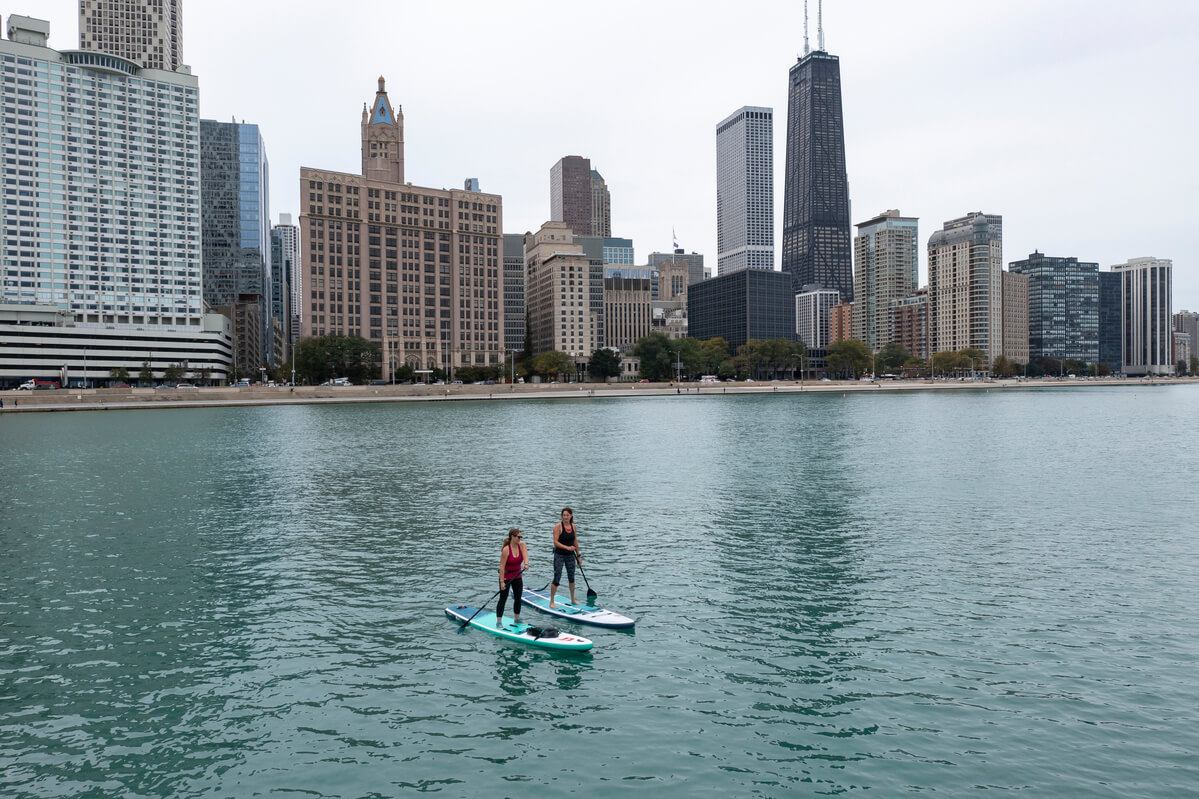 2 women paddle boarding with Chicago in the background