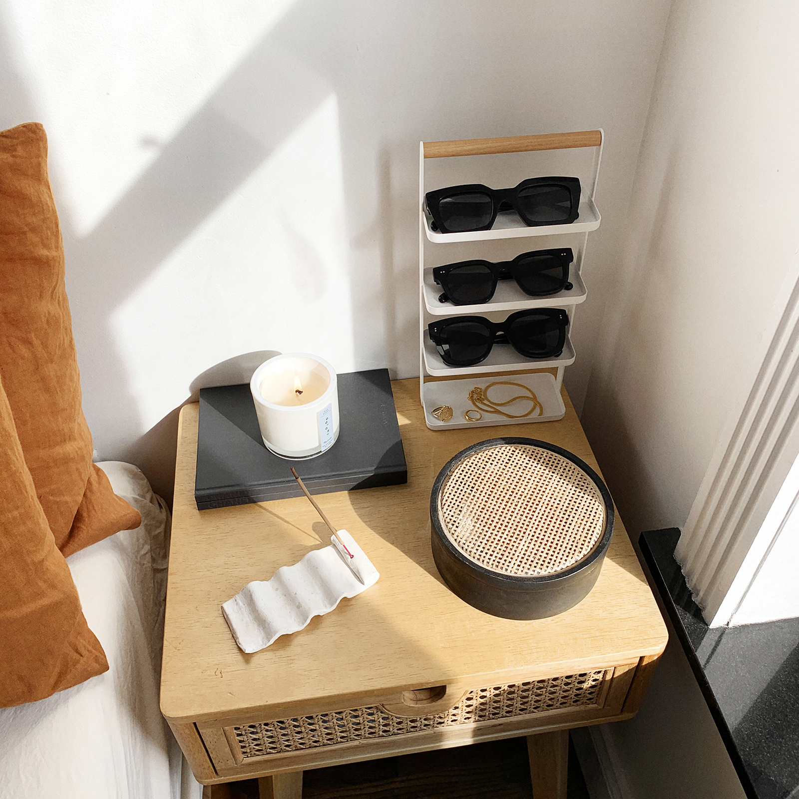 Aerial view of Yamazaki Home Tosca Jewelry and Accessory trays holding three of sunglasses and jewelry next to a candle and a book on a table. 