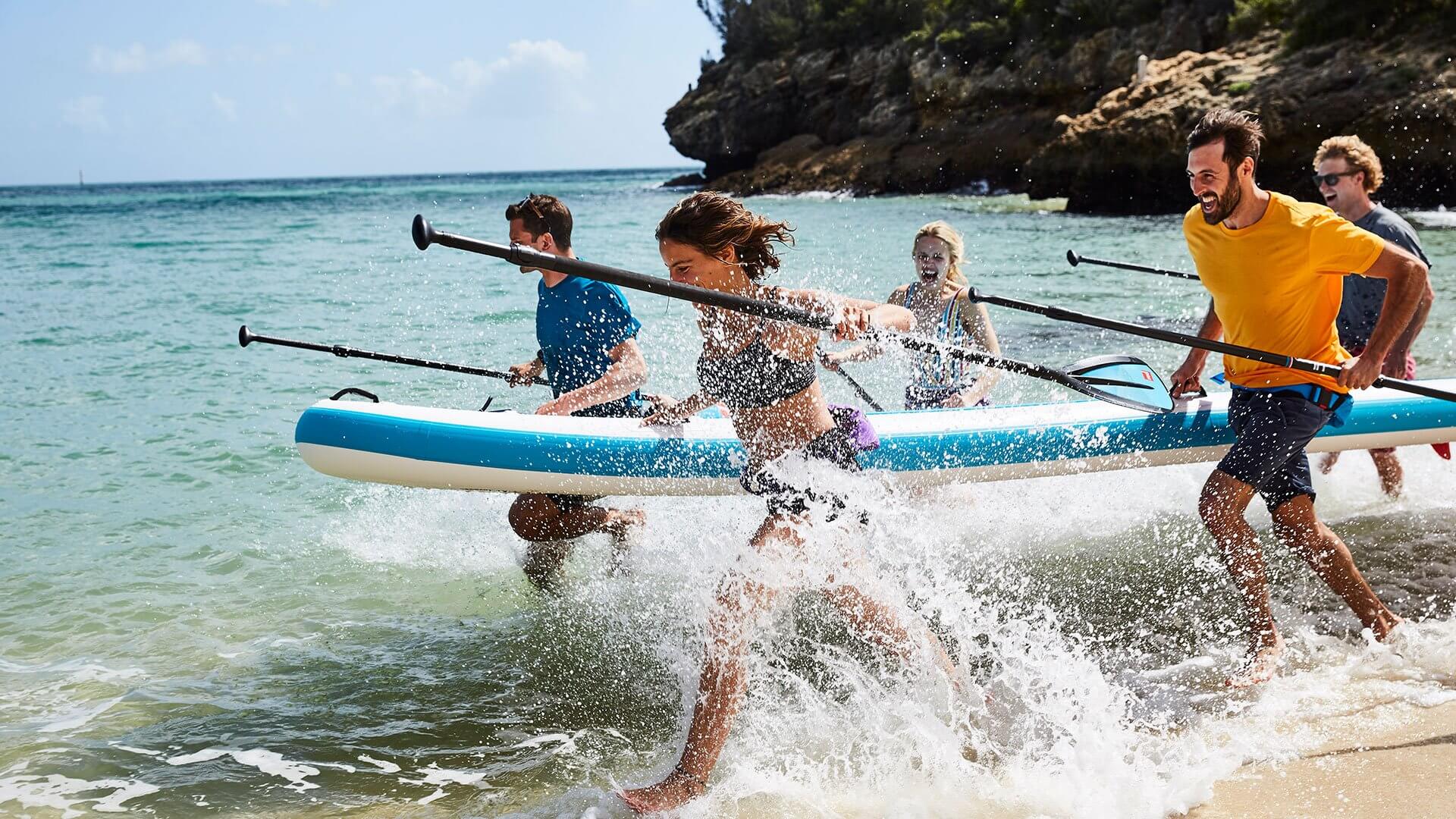 family running into the sea carrying a multi-person inflatable paddle board