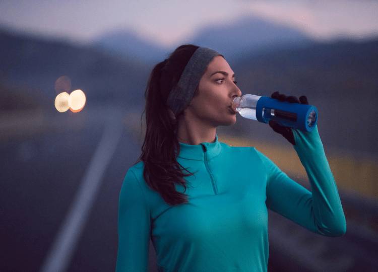 young female athlete standing on the pavement, drinking water and resting after exercising