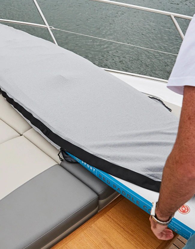 person storing paddle board inside uv board jacket on the deck of a boat