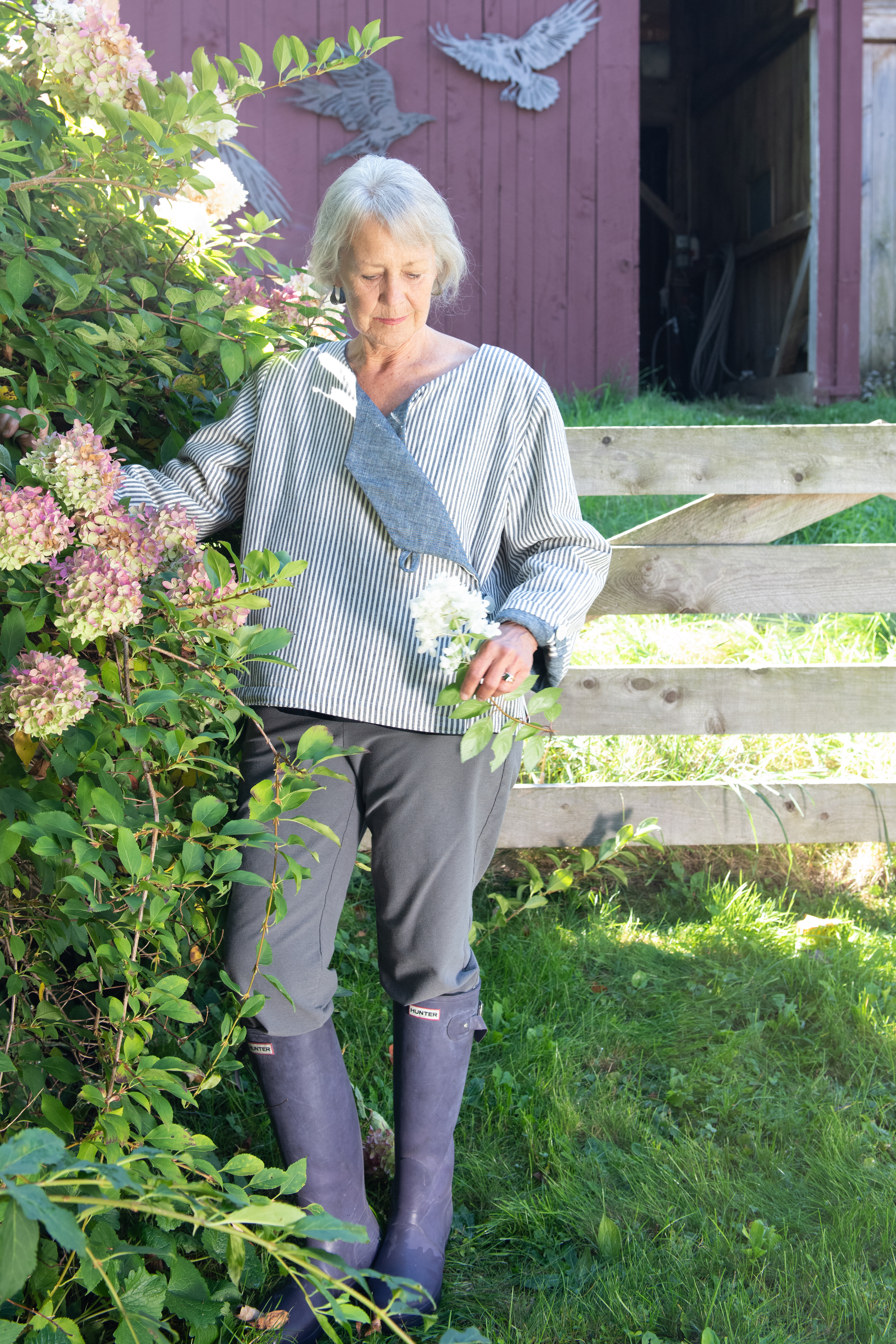 June, in the blue Latchkey jacket, standing next to hydrangeas and looking down