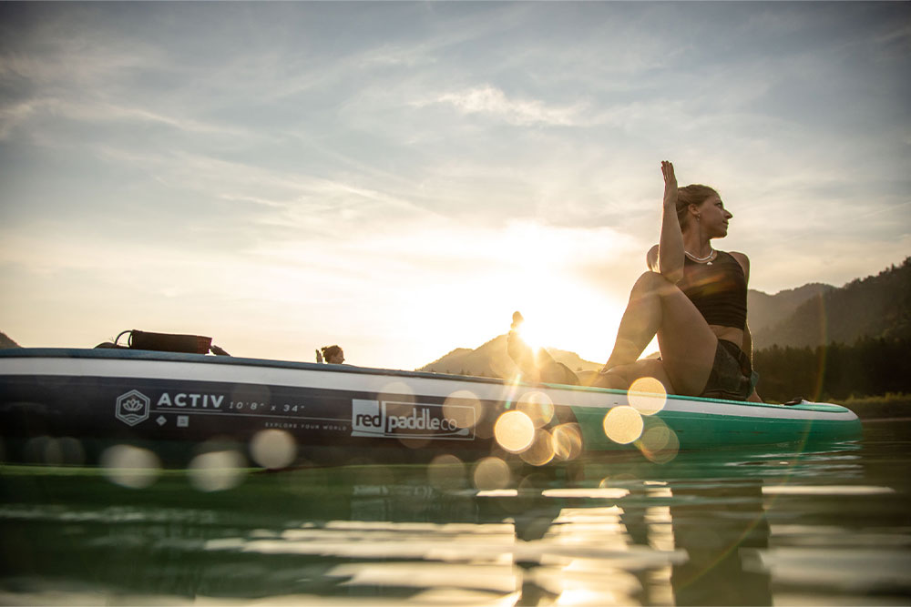 Woman sat on paddle board in a Yoga Pose
