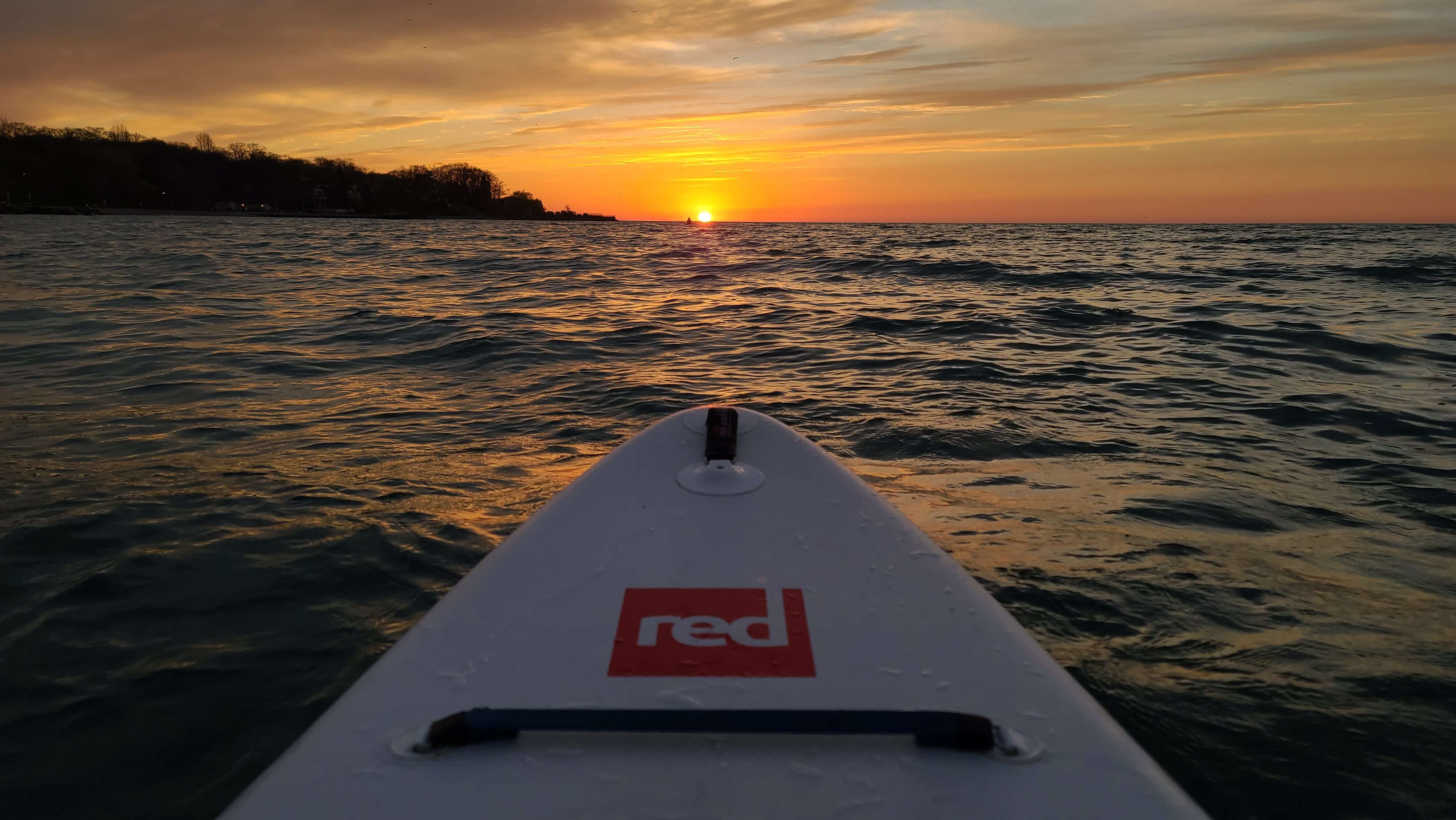 Red Original paddle board on a lake in the sunset