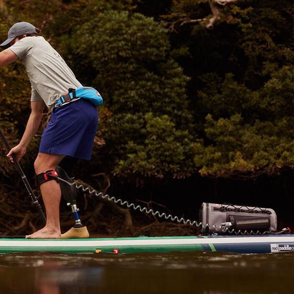Man paddling on lake using Red Original coiled SUP leash