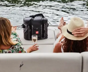 Two women on boat holding drinks with Red Original waterproof cool bag