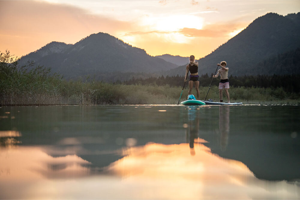 A woman and a man on their paddleboards paddling on a lake. 