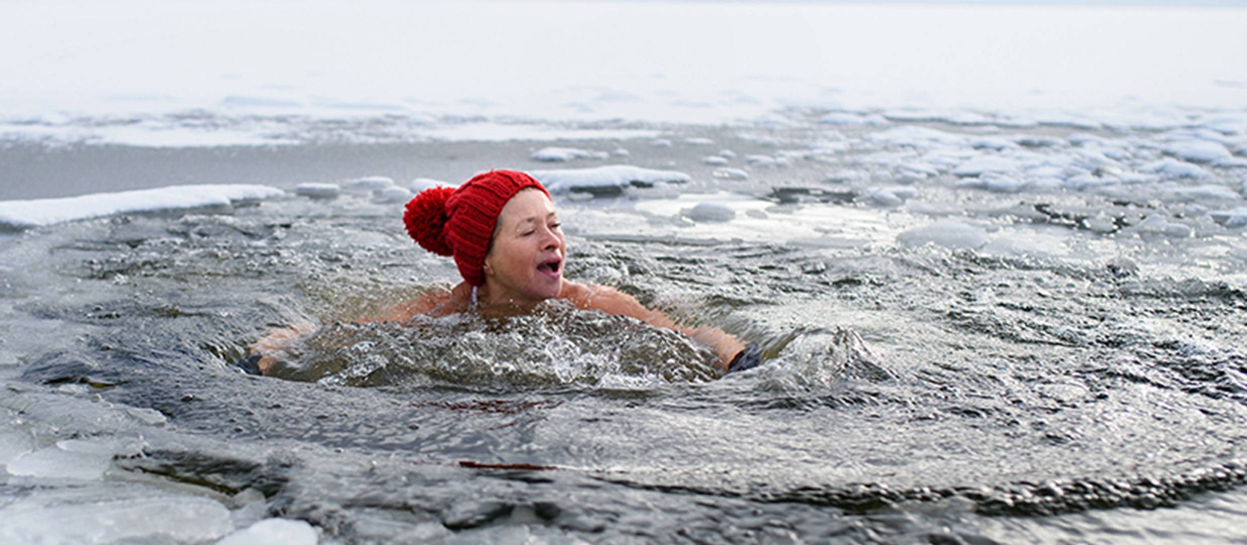 A woman swims in an icy lake to demonstrate the benefits of cold therapy