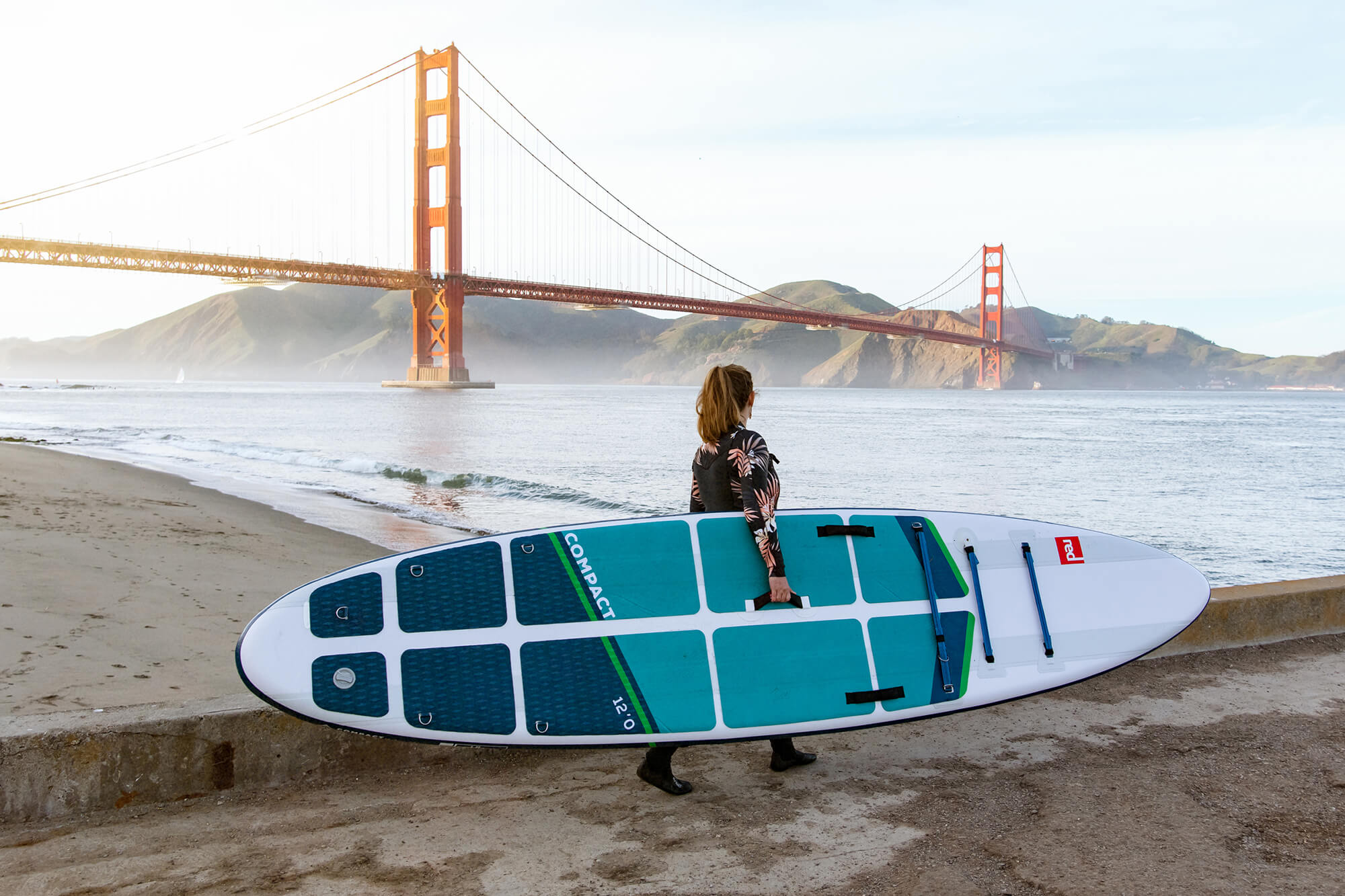 Close Shot Of Woman Carrying A Red Paddle SUP Along A Jetty In Front Of The Golden Gate Bridge