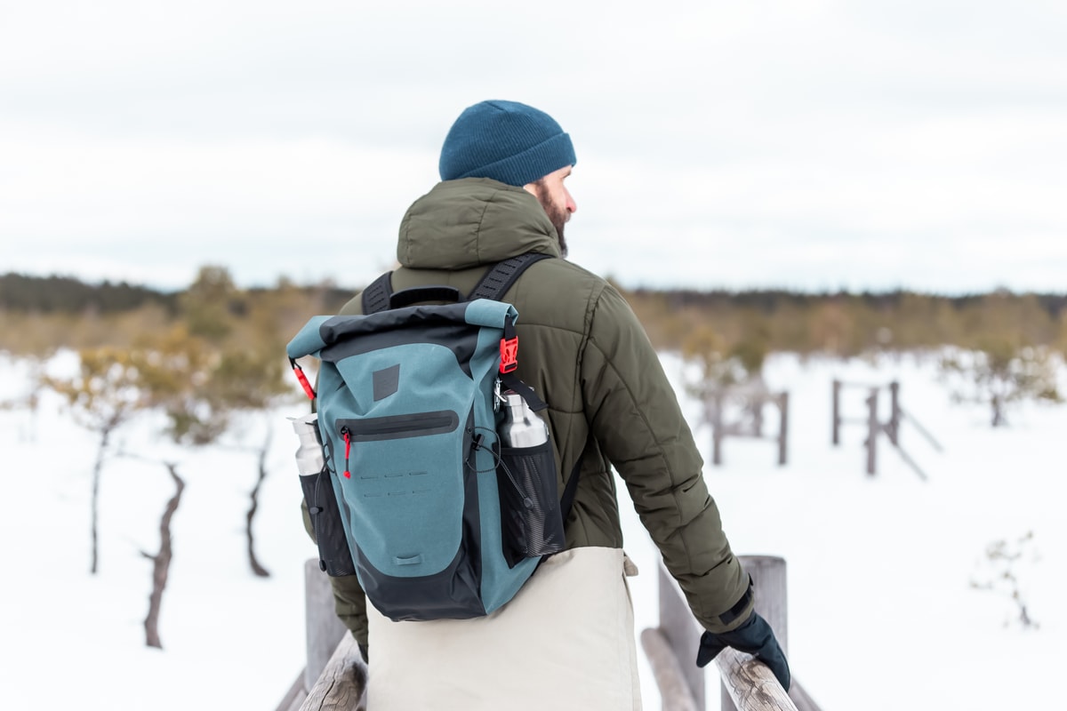 Man carrying a waterproof backpack and 2 insulated water bottles through a snowy landscape