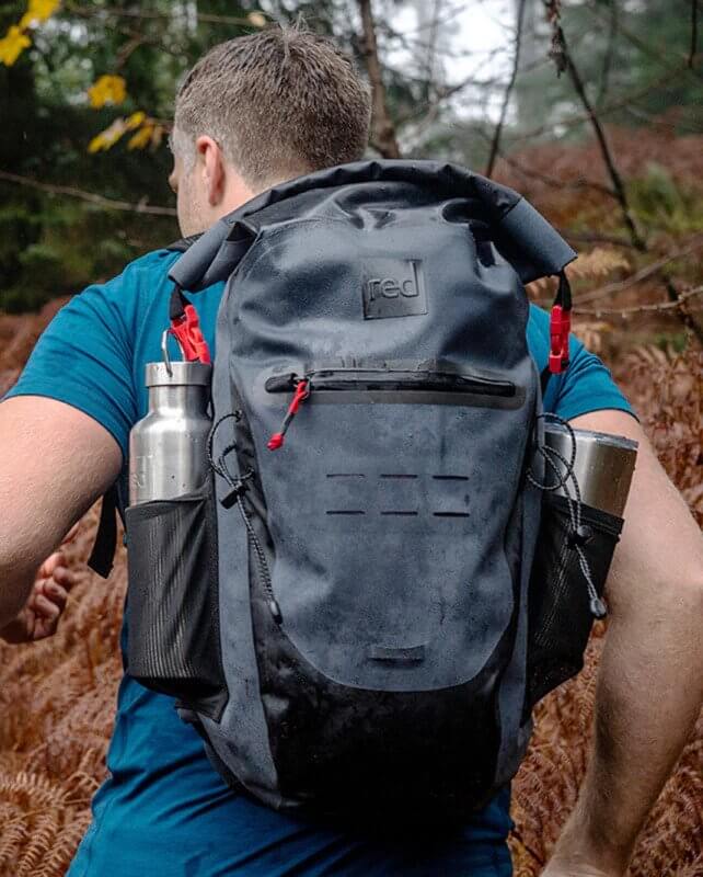 man wearing Red Original Waterproof Backpack whilst walking through a woodland area
