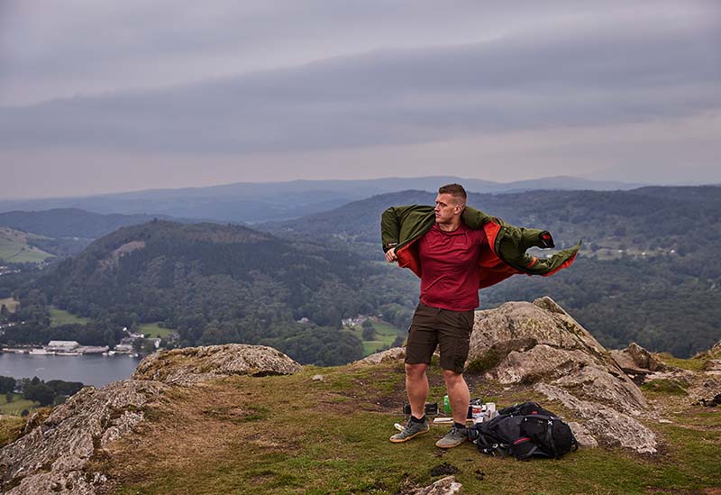 man putting changing robe on whilst standing on a windy mountain