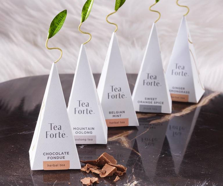 Five Winter Chalet pyramid tea infusers on a black reflective tray with a white fur background
