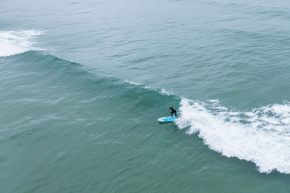 aerial view of person wearing a wetsuit catching a wave 