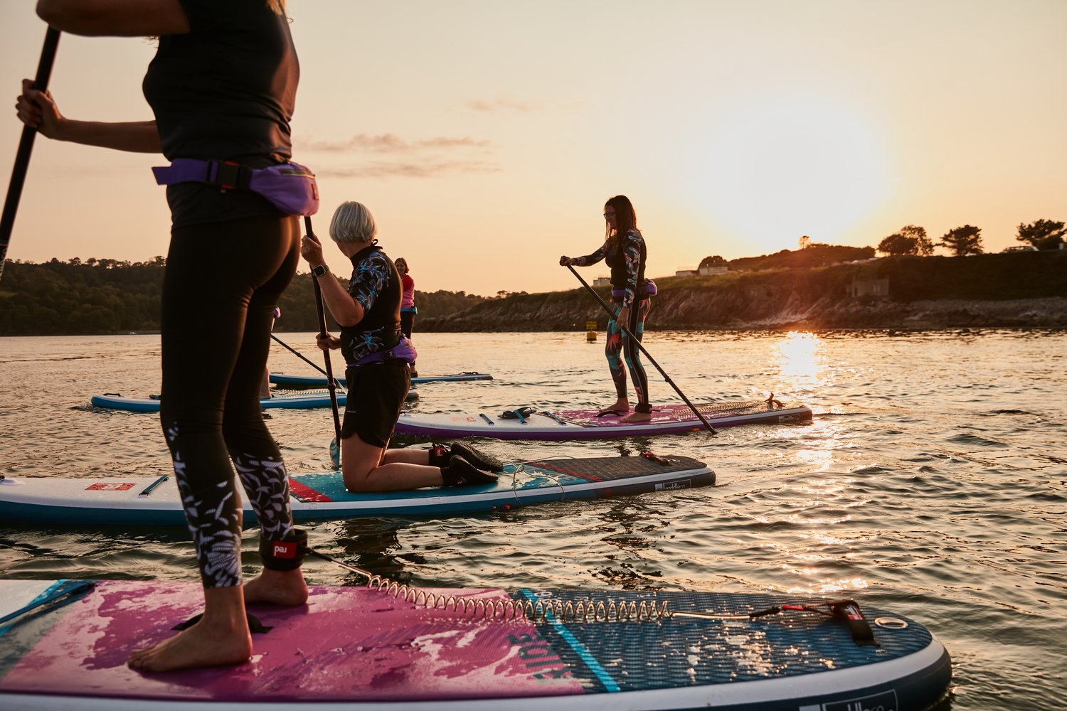 group of people stand up paddle boarding with one person kneeling and paddling
