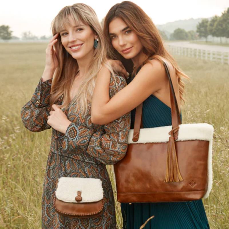 Two models in a field showcasing Patricia Nash sherpa and leather handbags