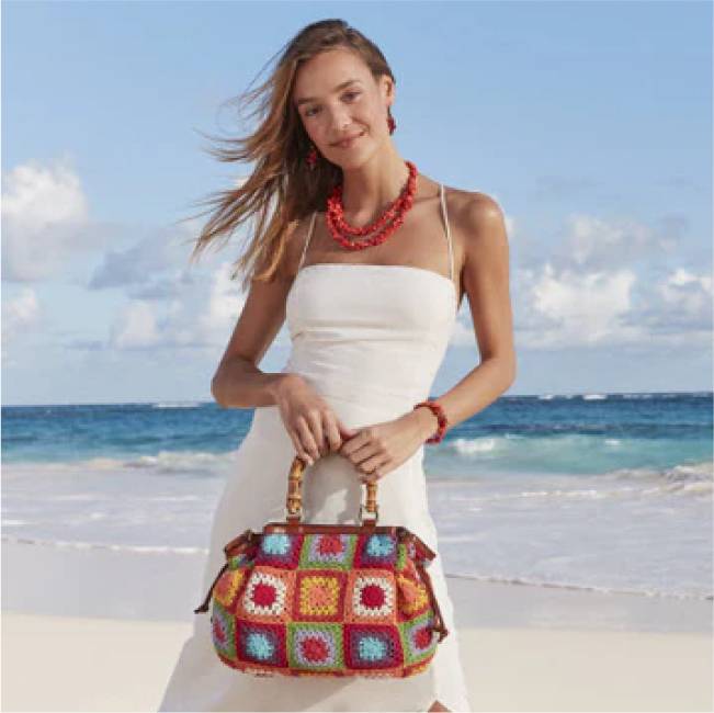 Model in white holding a Patricia Nash Patchwork handbag.