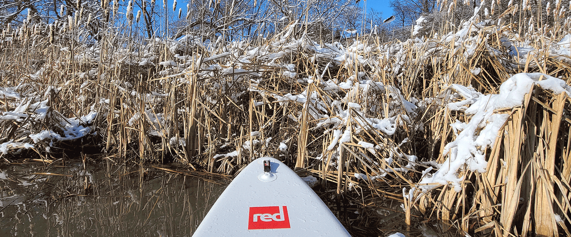 Die Spitze eines Red Paddleboards auf einem Gewaesser in einer Winterlandschaft
