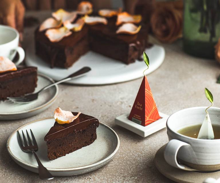 Slices of Cherry Blossom Infused Chocolate Torte on plates with tea and the full torte in the background