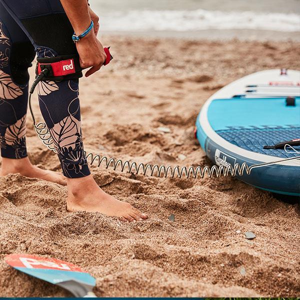 Person attaching Red Original coiled SUP leash to calf