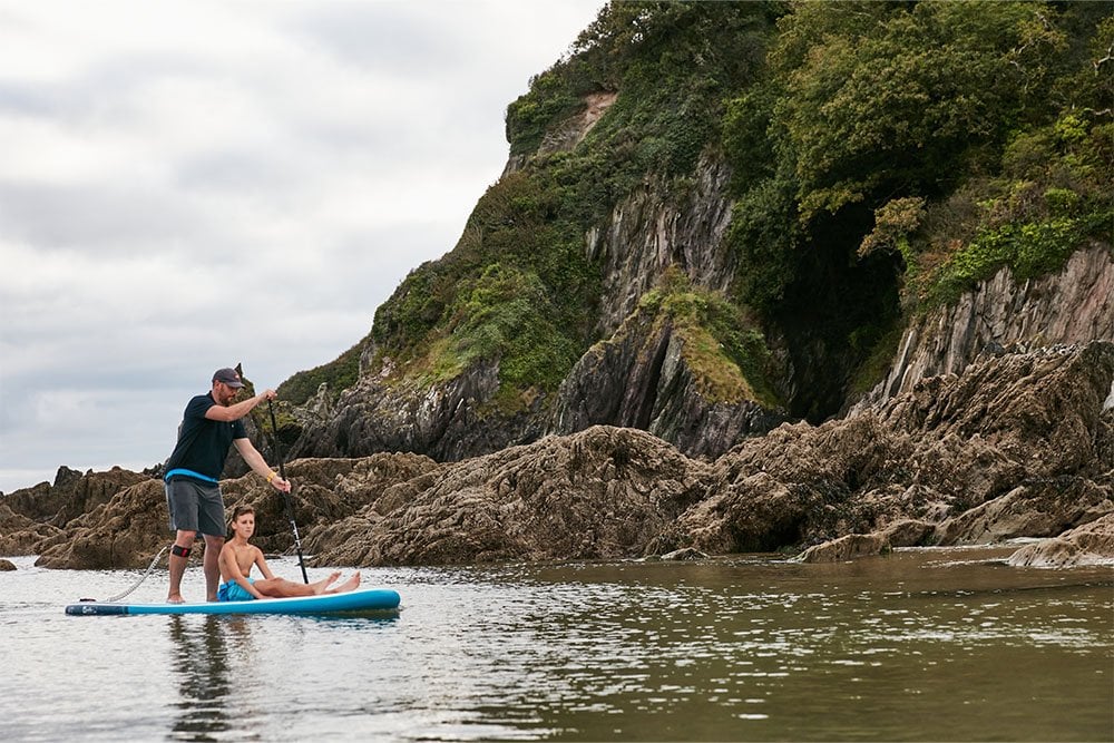 Man and child paddling a Red Original SUP near cliffs