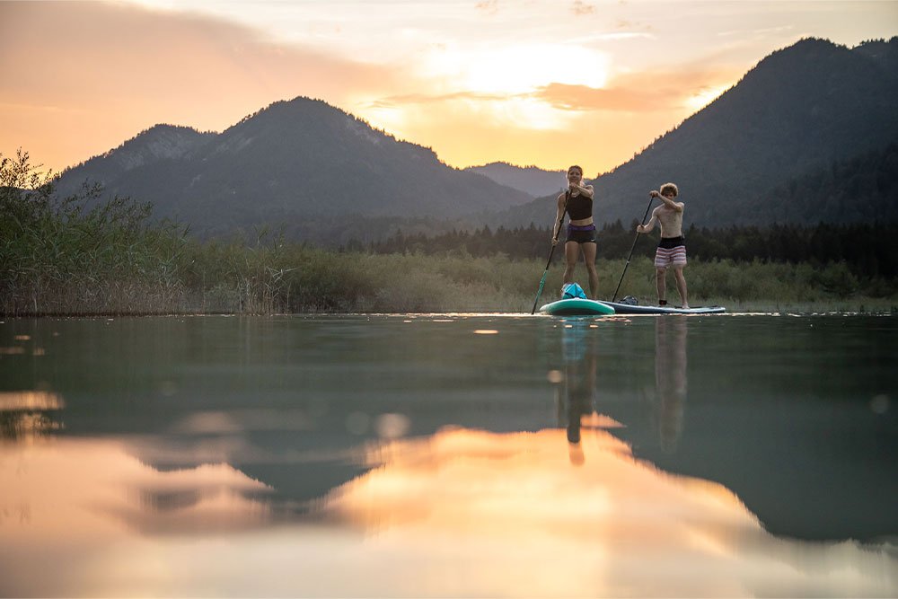 Two people paddle boarding on a lake in the sunset